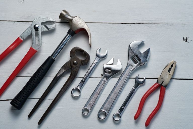 A variety of tools laid out on a white wooden table, emphasizing their unique forms and purposes.